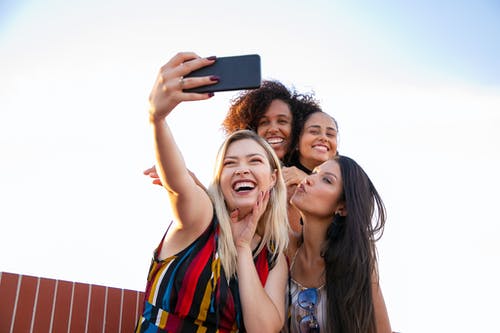 在智能手机上采取自拍照的开朗多种族女友 · 免费素材图片