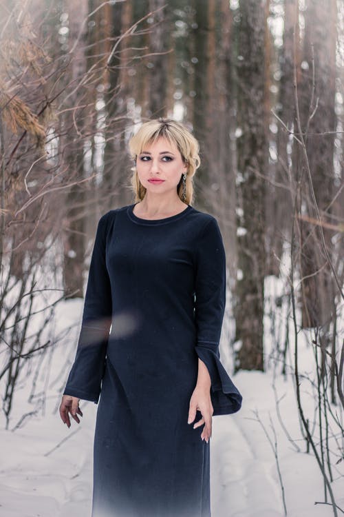女人站在白雪覆盖的土地上，周围绿树成荫 · 免费素材图片