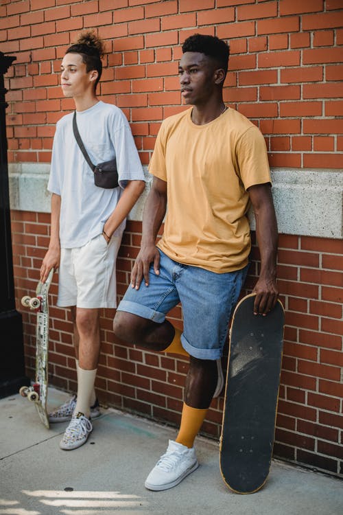 一起站立在砖墙附近的正面不同种族的男性溜冰者 · 免费素材图片