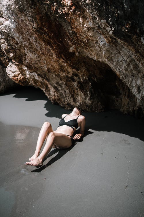 女人躺在岩石形成附近的沙子上 · 免费素材图片