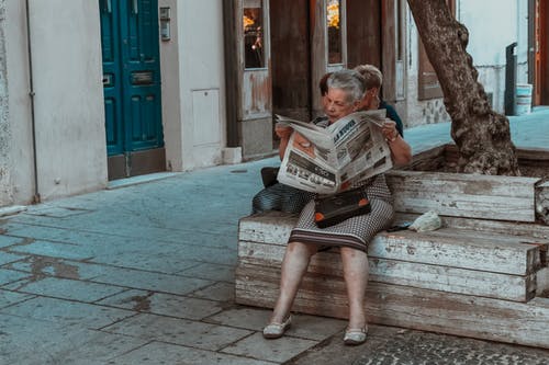 女人坐在板凳上看报纸 · 免费素材图片