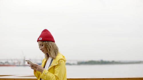 女人用她的智能手机站在水的附近 · 免费素材视频