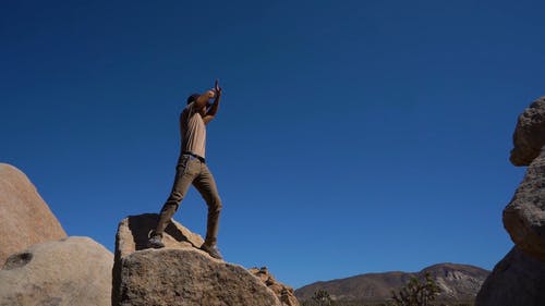 一个人站在一块巨石上挥舞着发出信号或要求注意的低角度镜头 · 免费素材视频