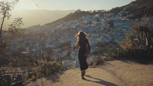 女人站在俯瞰城镇的山崖上 · 免费素材视频