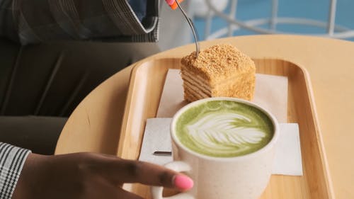 一个女人喜欢吃一杯拿铁咖啡旁边一个蛋糕在慢动作的木制托盘上的特写镜头 · 免费素材视频
