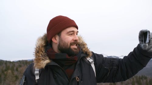 一名男子穿着冬季夹克和无檐小便帽的慢动作镜头，从手机拍摄周围的景色的视频 · 免费素材视频