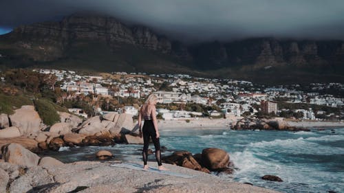 一个女人在俯瞰大海的岩石巨石上行使 · 免费素材视频