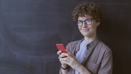 一个女人站在黑板前抱着她的手机 · 免费素材视频