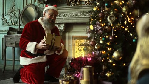 圣诞老人偷偷地把一盒礼物放在圣诞树下 · 免费素材视频