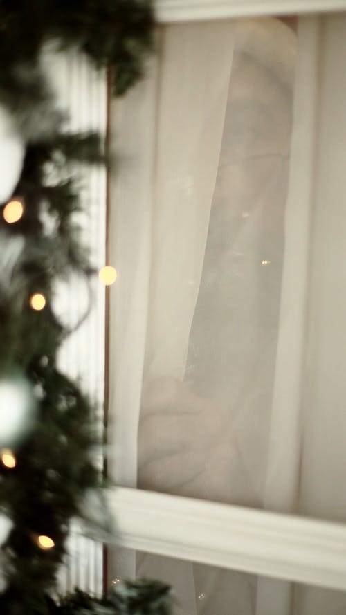 圣诞老人服装的一名老人窥视窗帘 · 免费素材视频
