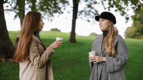两个站着的女人在喝咖啡时在公园聊天 · 免费素材视频
