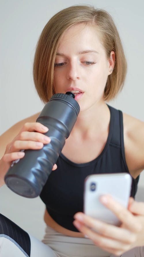 女人用她的智能手机，从一瓶水喝 · 免费素材视频