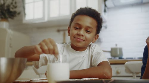 一个男孩在吃东西之前蘸着他在一杯牛奶中装饰的饼干 · 免费素材视频