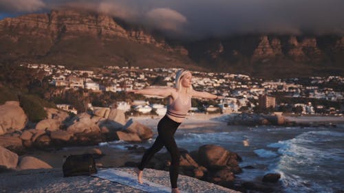一个女人在海边做瑜伽户外以一个村庄的景色的慢动作镜头 · 免费素材视频