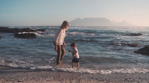 一位母亲帮助他的儿子从海滩岸边收集岩石 · 免费素材视频