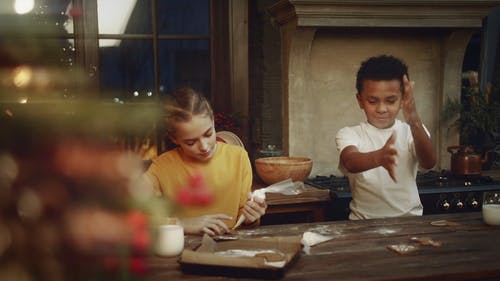 一个女孩把糖霜装饰放在饼干上，而旁边的男孩在他手上拍打发酵粉 · 免费素材视频