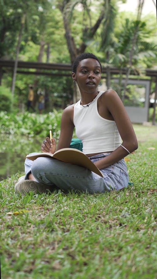 一个女人坐在草地上，一边学习 · 免费素材视频