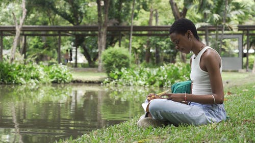 一个女人在学习笔记时坐在池塘边的草地上 · 免费素材视频