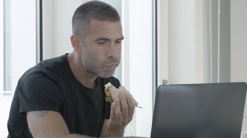 一个人在手边用一台笔记本电脑用三明治工作 · 免费素材视频